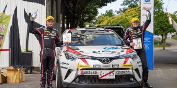 Mike Young and Amy Hudson standing on podium with Toyota TRD CH-R rally car