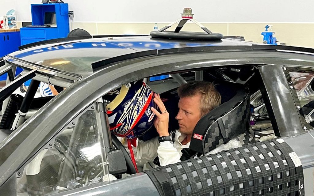 Kimi Raikkonen sitting in NASCAR putting helmet on