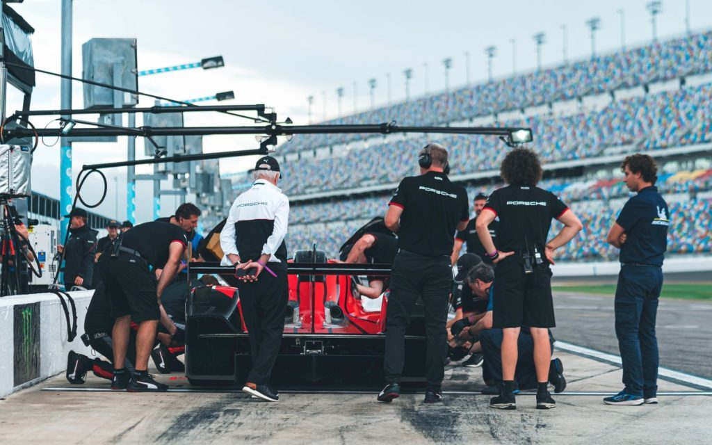 People standing around Porsche 963 in pit lane