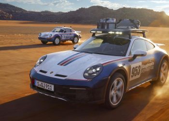 Porsche 911 Dakar next to 1984 rally car driving off-road front three quarter view