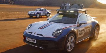 Porsche 911 Dakar next to 1984 rally car driving off-road front three quarter view