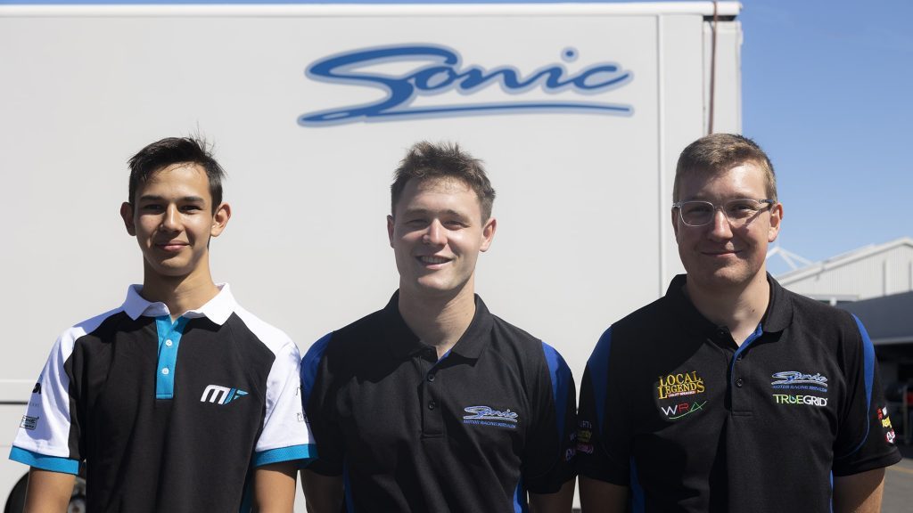 Ronan Murphy, Marcus Flack, and Harrison Goodman standing in front of Sonic Racing trailer